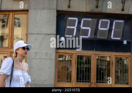 Moscou, Russie. 24 juin 2021 UNE femme marche dans la rue Tverskaya, dans le centre de Moscou, sur fond d'un panneau d'information sur le bâtiment du télégraphe central montrant une température de l'air de 35°С. Le 24 juin 2021, la température de jour devrait atteindre +36°С [96,8°F]. Un avertissement météo orange a été émis en raison de l'onde de chaleur Banque D'Images