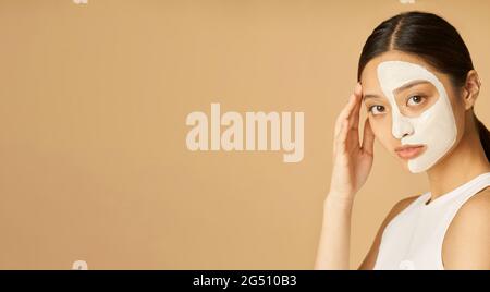 En-tête de site Web de Studio photo de jeune femme avec masque facial appliqué sur la moitié de son visage regardant la caméra, recevant des soins spa isolés plus Banque D'Images