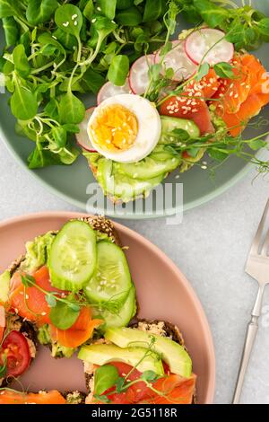 Petit déjeuner sain et savoureux, sandwichs à l'avocat et au saumon, concombres et tomates, radis et microverts de petits pois avec œufs durs et salade de racines Banque D'Images