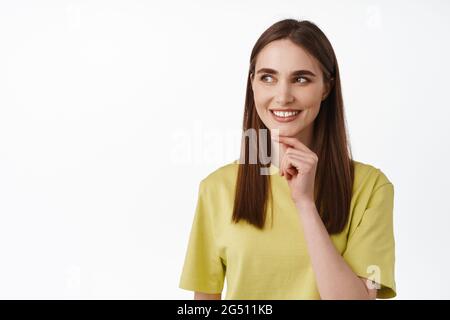 HMM intéressant, laissez-moi penser. Sourire fille toucher le menton et de penser, regardant de côté à la proposition et de réfléchir acheter ou non, en butant contre blanc Banque D'Images