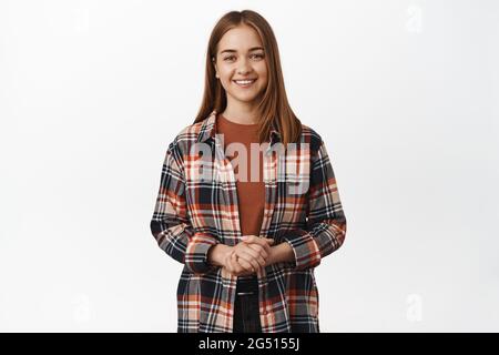 Portrait d'une fille caucasienne amicale et polie, assistante de femme serviable souriant agréable, tenant les mains serrées sur la poitrine, debout contre Banque D'Images