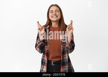 Image d'une femme excitée espérant le sourire, croiser les doigts, sourire avec les yeux fermés, mendiant la fortune de rêver se réaliser, anticipant, se tenant contre Banque D'Images