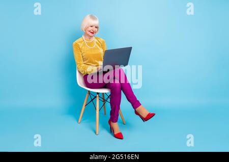 Pleine photo de positif court coiffure dame aînée s'asseoir travail ordinateur portable porter chemisier pantalon isolé sur fond bleu de couleur Banque D'Images