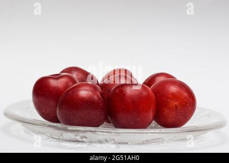 Prunes rouges biologiques crues sur fond blanc, tons de marron rouge, fruits frais brillants. Fruits de la ferme frais bio prunes rouges produits récoltés.servi dans l'assiette sur wh Banque D'Images