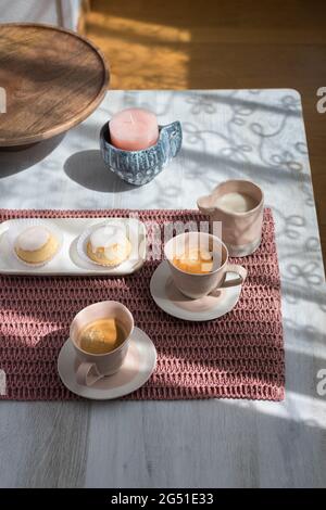 Petit déjeuner rose paisible pour deux servi sur une nappe rose avec deux tasses de café, un goûter avec deux gâteaux au citron et un pot de lait sur une table en bois. Banque D'Images