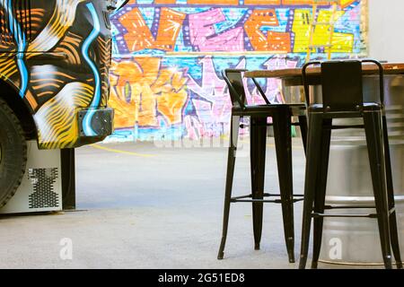 Tabourets de bar élégants en métal noir, table en métal contre un graffiti coloré. Un emplacement urbain industriel moderne pour se détendre en été. Nourriture t Banque D'Images