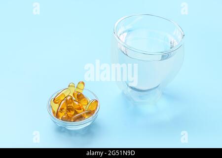 Bol avec capsules d'huile de poisson et verre d'eau sur fond de couleur Banque D'Images