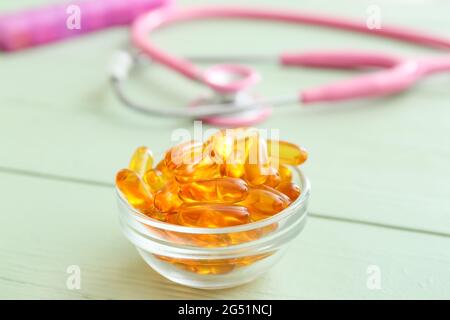 Bol avec capsules d'huile de poisson et stéthoscope sur fond en bois de couleur Banque D'Images