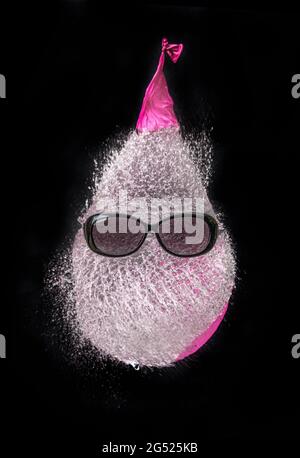 Une photo amusante. Un ballon rempli d'eau éclate. L'eau est en forme de tête et a des lunettes de soleil dessus Banque D'Images