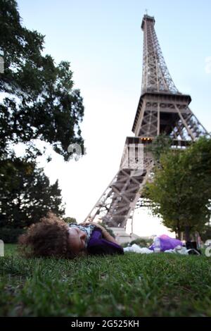 Une jeune femme en voyage d'été, couchée sur une pelouse verdoyante près de la Tour Eiffel Banque D'Images