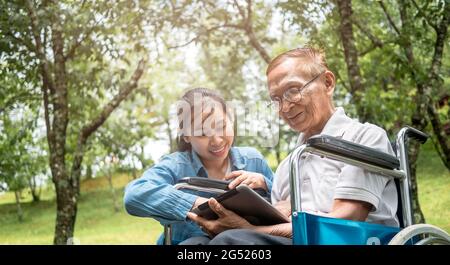 Grand-père en fauteuil roulant et petite-fille s'amuser avec une tablette numérique dans le parc. La vie de famille en vacances. Banque D'Images