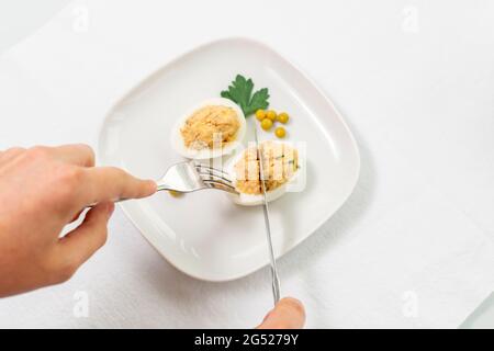 œufs farcis avec du thon en conserve et des herbes. l'homme coupe un morceau d'œuf Banque D'Images