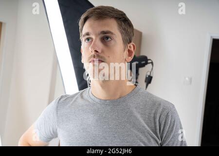 Jeune beau grand homme blanc mince avec des cheveux bruns regardant vers le haut en studio de photo en chemise grise Banque D'Images