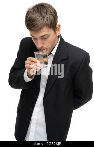 Jeune beau grand blanc mince homme avec des cheveux bruns mettant la langue dans le verre de l'eau dans blazer noir isolé sur fond blanc Banque D'Images