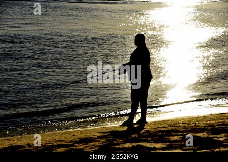 HOMME PÊCHE DEPUIS LA PLAGE AU COUCHER DU SOLEIL Banque D'Images