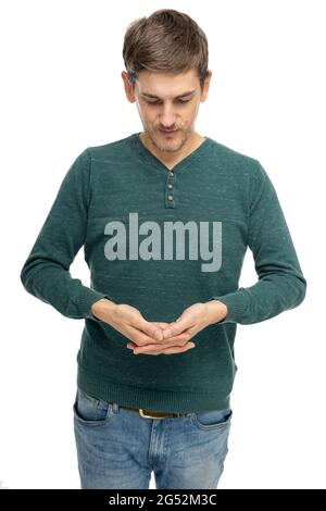 Jeune beau grand homme blanc mince avec des cheveux bruns regardant vers le bas à ses mains jointes dans le chandail vert foncé isolé sur fond blanc Banque D'Images