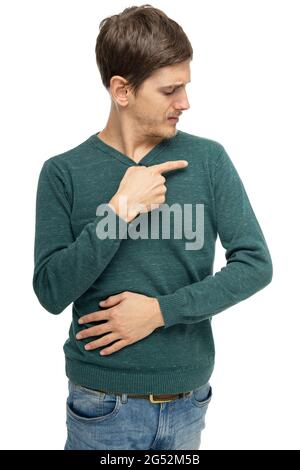 Jeune beau grand homme blanc mince avec des cheveux bruns pointant vers son épaule dans un chandail vert foncé avec des jeans bleus isolés sur fond blanc Banque D'Images