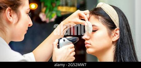 Vue latérale d'un maquilleur utilisant un aérographe faisant une base de maquillage d'aérographe sur un visage de femme dans un salon de beauté Banque D'Images
