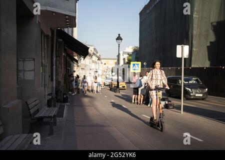 Moscou, Russie - 21 juin 2021, UNE fille de brune vêque d'un scooter électrique se déplace le long de la rue Bolshaya Nikitskaya le long d'une piste cyclable Banque D'Images