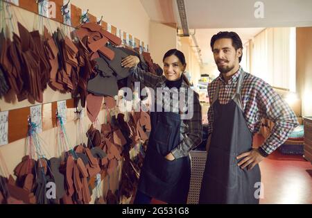 Portrait des travailleurs heureux de l'usine de chaussures debout près des crochets cintres avec des détails en cuir Banque D'Images