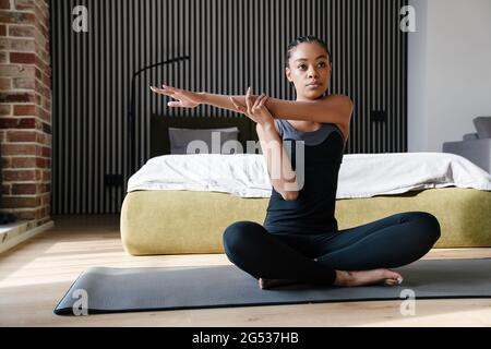 Belle jeune femme africaine en bonne santé faisant des exercices de yoga sur un tapis de fitness dans la chambre, positions de yoga Banque D'Images