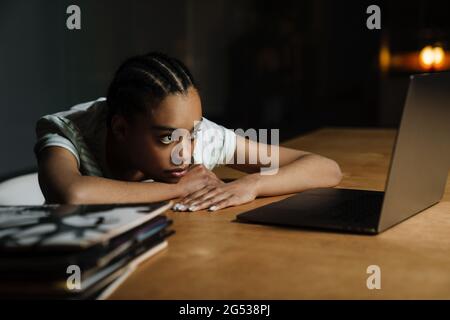 Femme noire fatiguée travaillant avec un ordinateur portable tout en étant assise à une table au bureau Banque D'Images