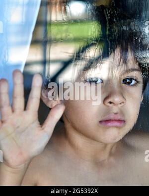 Titre enfant triste et angoissé regardant derrière le verre humide avec la main reposant sur la fenêtre Banque D'Images