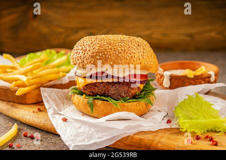 Délicieux hamburger et frites chaudes prêts à consommer. Une planche à découper en bois de mangue dans un style rustique. Salade d'herbes fraîches et d'arugula. Profitez de votre Banque D'Images