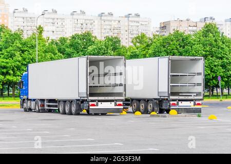 Deux camions dans un stationnement avec une remorque à conteneur vide ouvrent des portes à l'arrière, prêts à charger des produits, des marchandises Banque D'Images