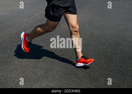 jambes coureur homme dans des chaussures orange vif courir sur l'asphalte foncé Banque D'Images