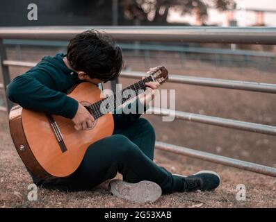 garçon jouant la guitare classique assis sur le sol dans un carré en automne dans des vêtements décontractés, horizontal, point sélectif de l'espace de copie Banque D'Images