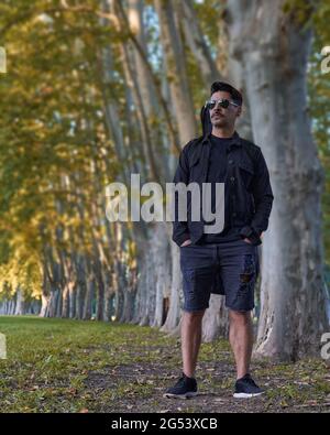 garçon marchant au milieu de la forêt avec sa guitare dans sa gaine sur son épée, vêtu de vêtements décontractés noirs, sélectif focus, espace de copie verti Banque D'Images