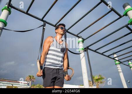 Un athlète masculin s'entraîne dans une salle de sport en plein air avec des anneaux. Jeune homme musclé attrayant pendant un entraînement. Banque D'Images