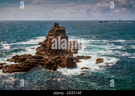 La mer tourbillonne autour de la formation rocheuse du Chevalier armé, à la fin du Land à Cornwall, avec le phare des Longships au loin. Banque D'Images