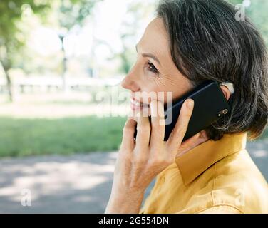 Une femme mature avec une prothèse auditive a une vie entière et peut entendre son interlocuteur au téléphone. Solution auditive et technologie innovante Banque D'Images