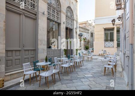 Pause-café à l'île d'Ermoupolis Syros, Cyclades, Grèce. Vue sur le café restaurant, tables chaises sur une allée pavée vide entre néoclassique Banque D'Images