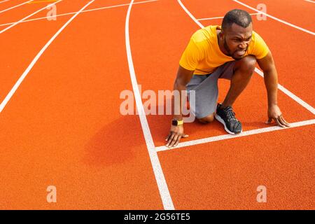 Homme sportif pensif se focalise et se prépare à l'entraînement à la course. Athlète afro-américain de course debout sur la ligne de départ prêt à courir rapidement, se préparant Banque D'Images