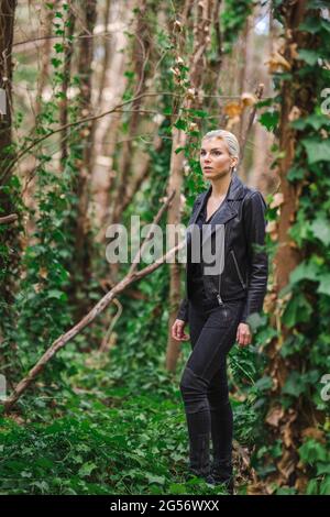 La mode dans des endroits insolites, jeune femme dans la veste de moto ébougée dans la forêt Banque D'Images