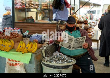 Homme géorgien en surpoids. Un vendeur de rue lit un journal tout en étant assis au comptoir. Banque D'Images