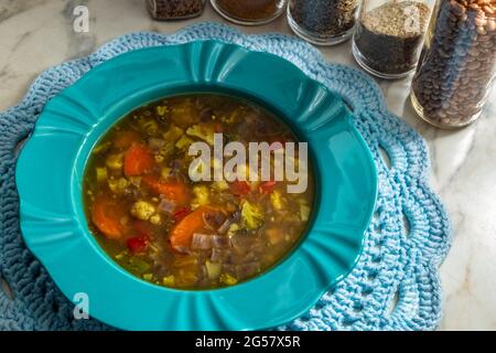 Un plat vert, rempli de soupe de légumes, sur un mousplat crocheté. Verres aux épices composant la photo. Banque D'Images