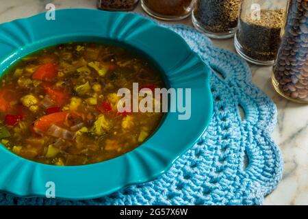 Un plat vert, rempli de soupe de légumes, sur un mousplat crocheté. Verres aux épices composant la photo. Banque D'Images