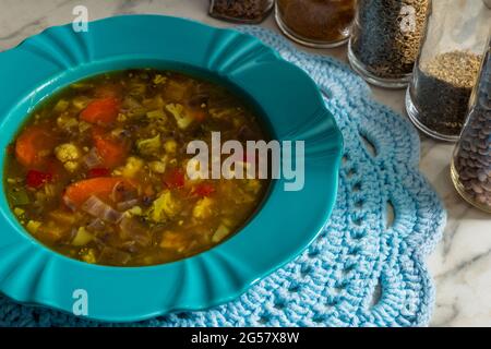 Un plat vert, rempli de soupe de légumes, sur un mousplat crocheté. Verres aux épices composant la photo. Banque D'Images