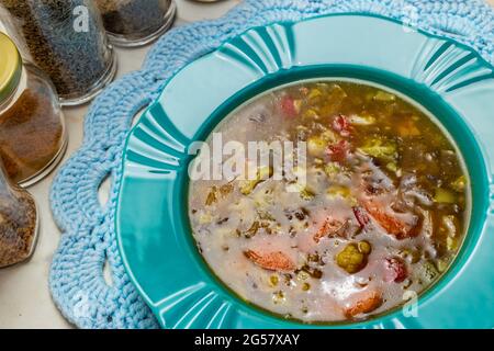 Un plat vert, rempli de soupe de légumes, sur un mousplat crocheté. Verres aux épices composant la photo. Banque D'Images