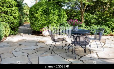 Patio en fer forgé sur un patio en pierre avec jardin formel. Banque D'Images