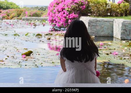 Petite fille assise près de l'étang de fleurs de nénuphars dans un complexe à Bali, Indonésie Banque D'Images