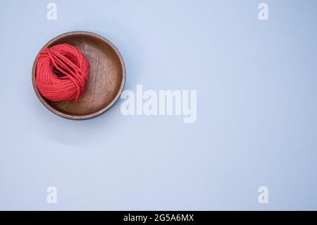 Vue de dessus du fil rouge pour tricoter dans un bol en bois sur fond bleu Banque D'Images