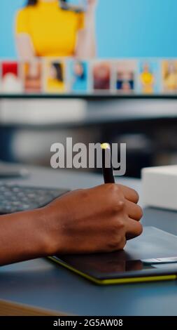 Gros plan de retouche photo africaine tenant un stylet retouche photo de client à l'aide d'un ordinateur avec deux écrans. Éditeur graphique retouche des ressources de dessin sur tablette graphique dans un bureau d'agence de création Banque D'Images