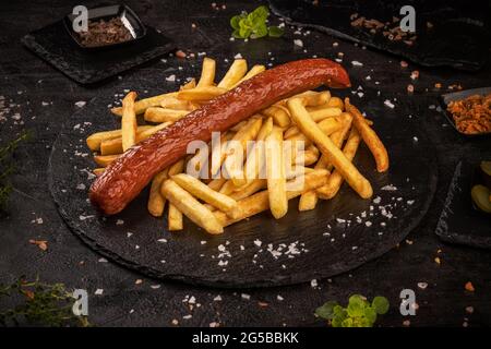 Saucisses de porc grillées servies avec des frites sur fond d'ardoise noire Banque D'Images