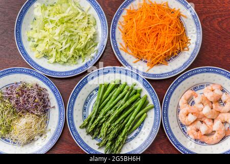 Crevettes, asperges vertes, carottes, laitue iceberg et luzerne sur une table en bois Banque D'Images