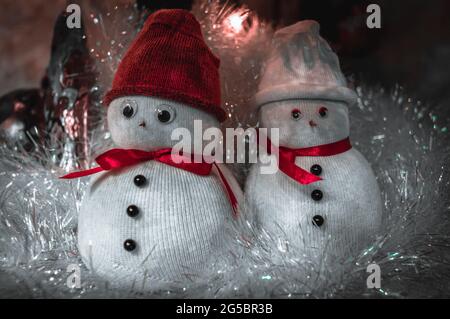 Bonhommes de neige mignons en casquettes recouverts de guirlande à Noël. Banque D'Images